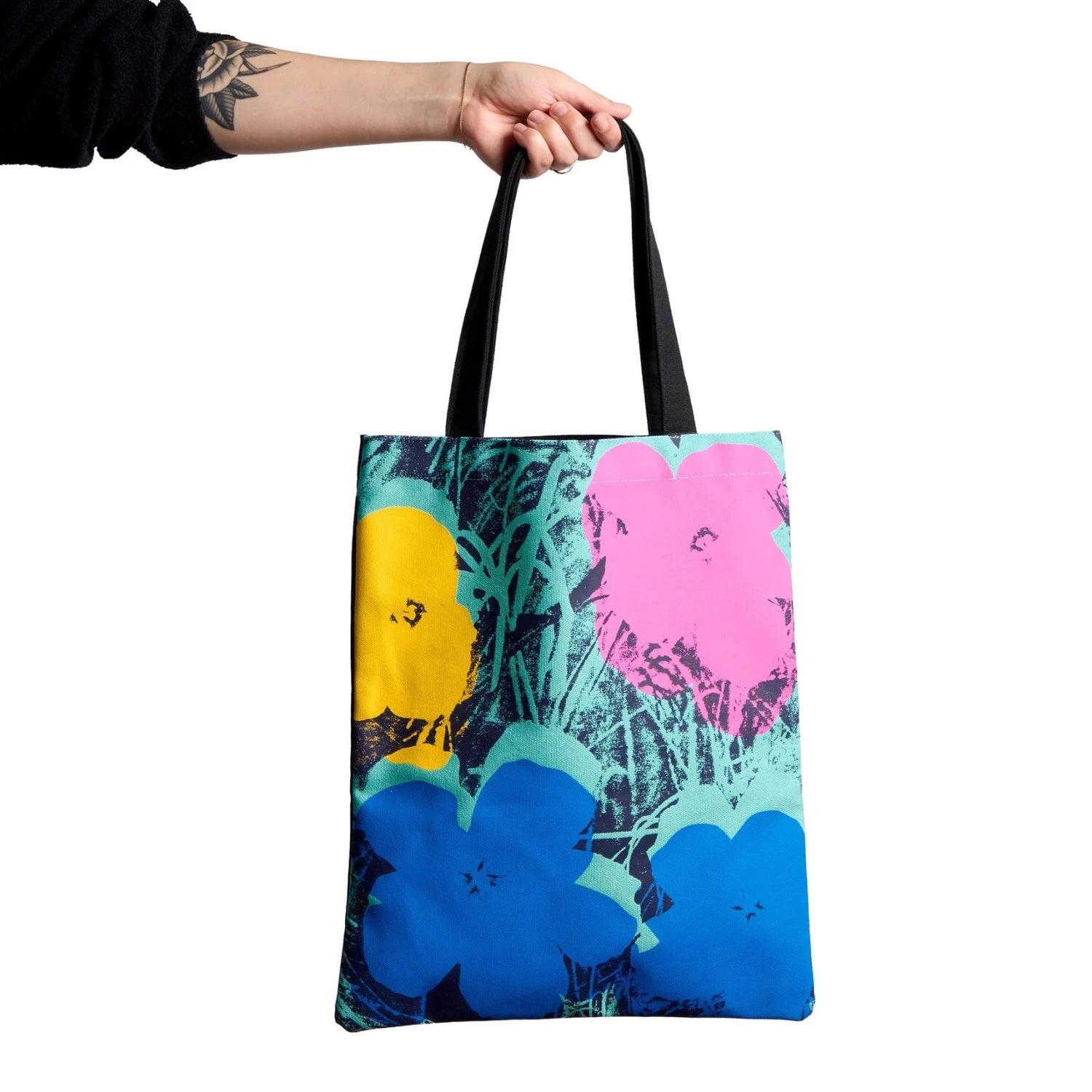 Tote bag with colorful Andy Warhol pop art floral design held by a person against a white background