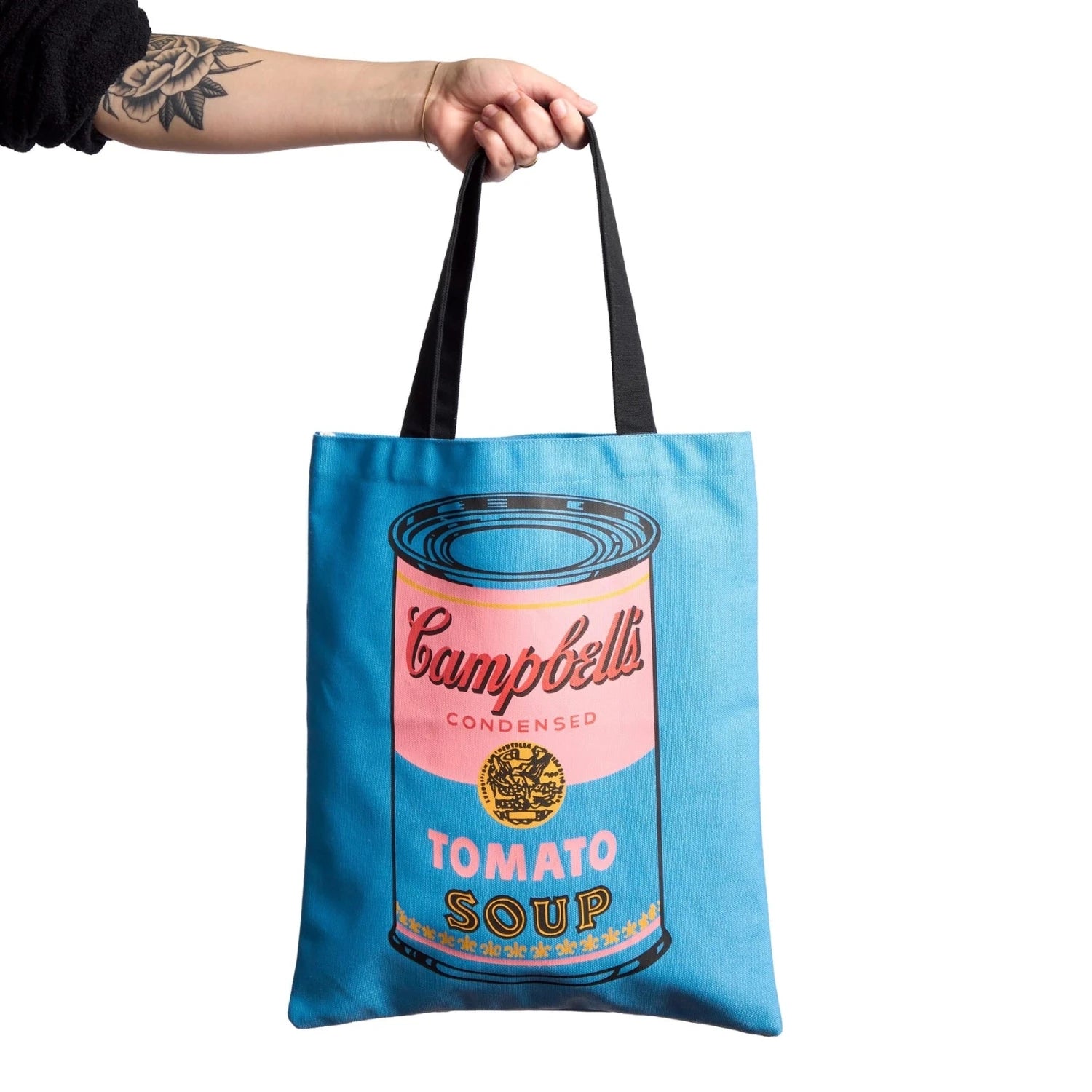Blue Tote bag with pop art Campbell's Tomato Soup design held by a hand on a white background