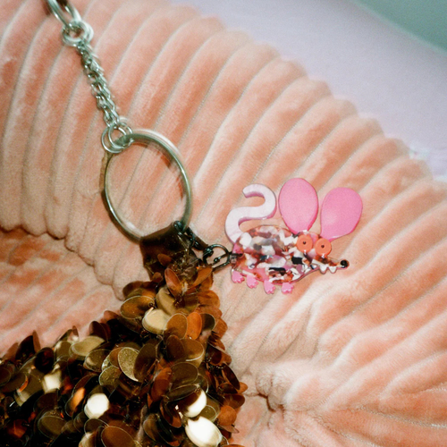 Keychain of a pink baby rat design on a textured surface