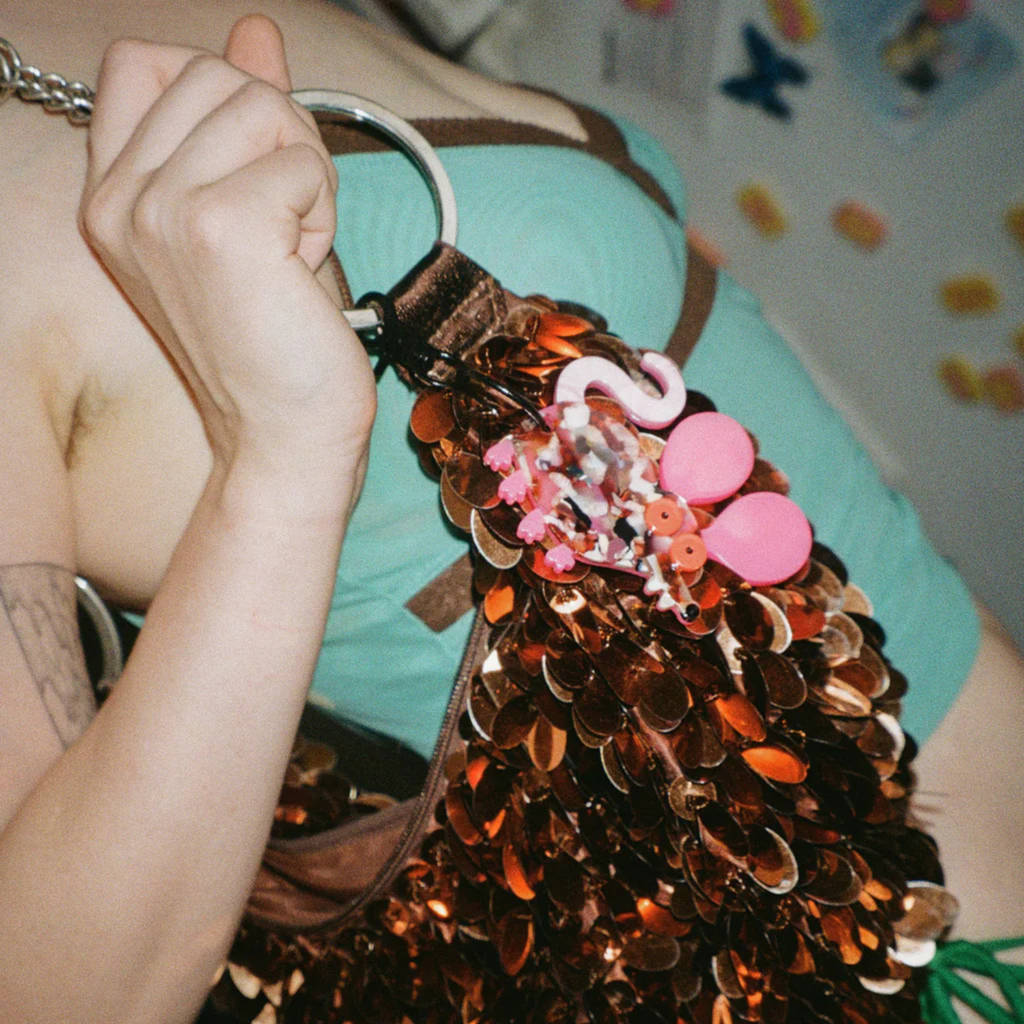 Person holding a decorative bag with sequins and pink rat keychain attached.