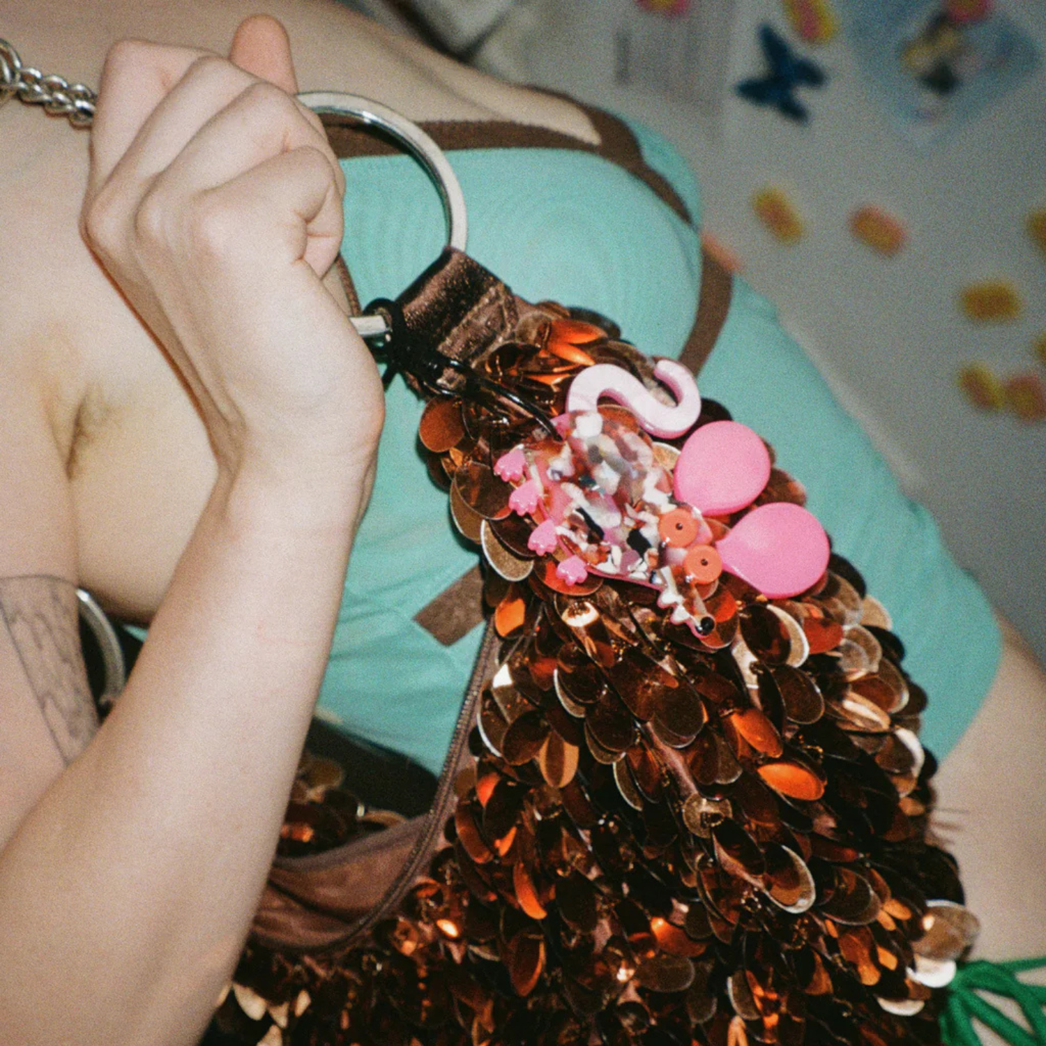 Person holding a decorative bag with sequins and pink rat keychain attached.