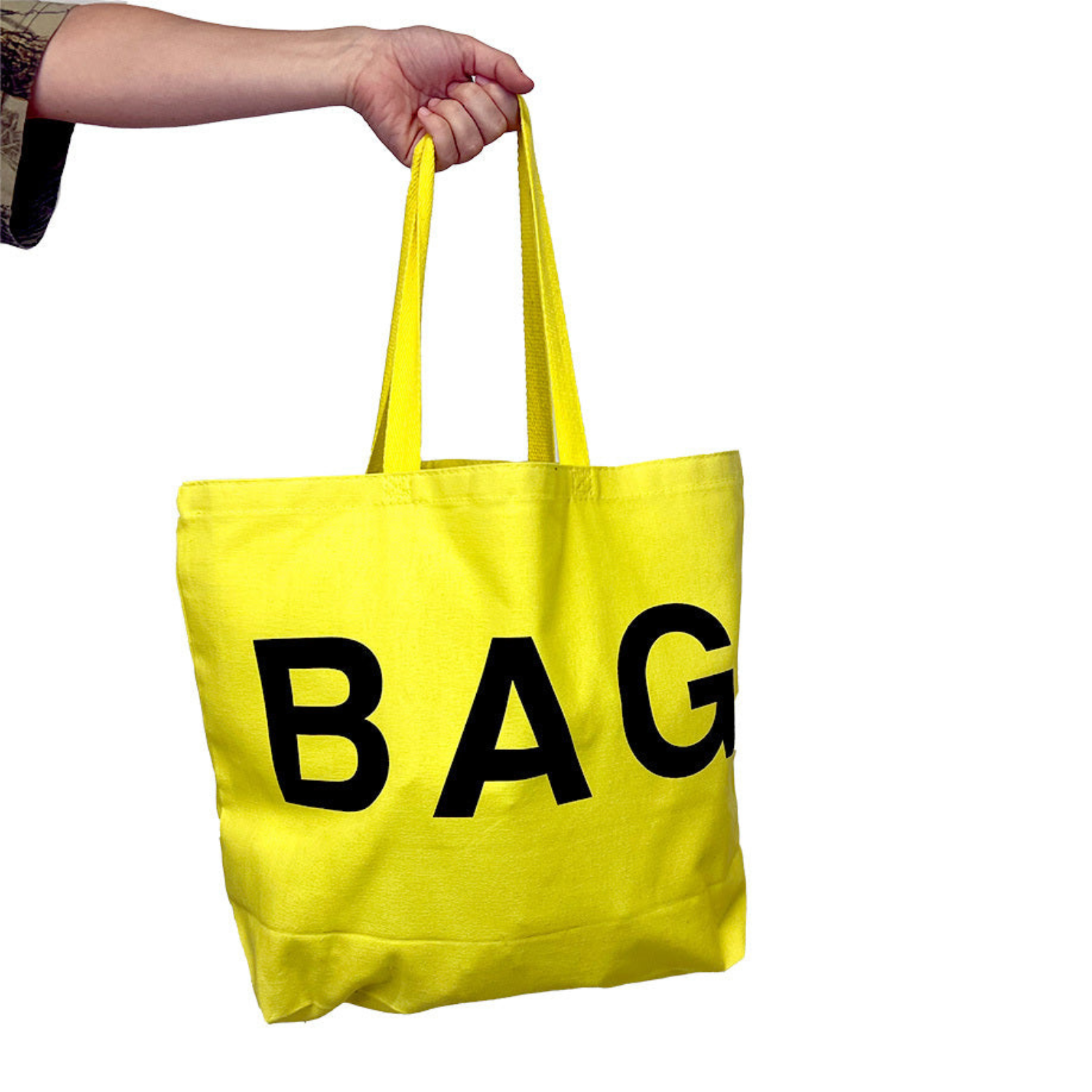 Yellow tote bag with 'BAG' printed on it held by a person against a white background