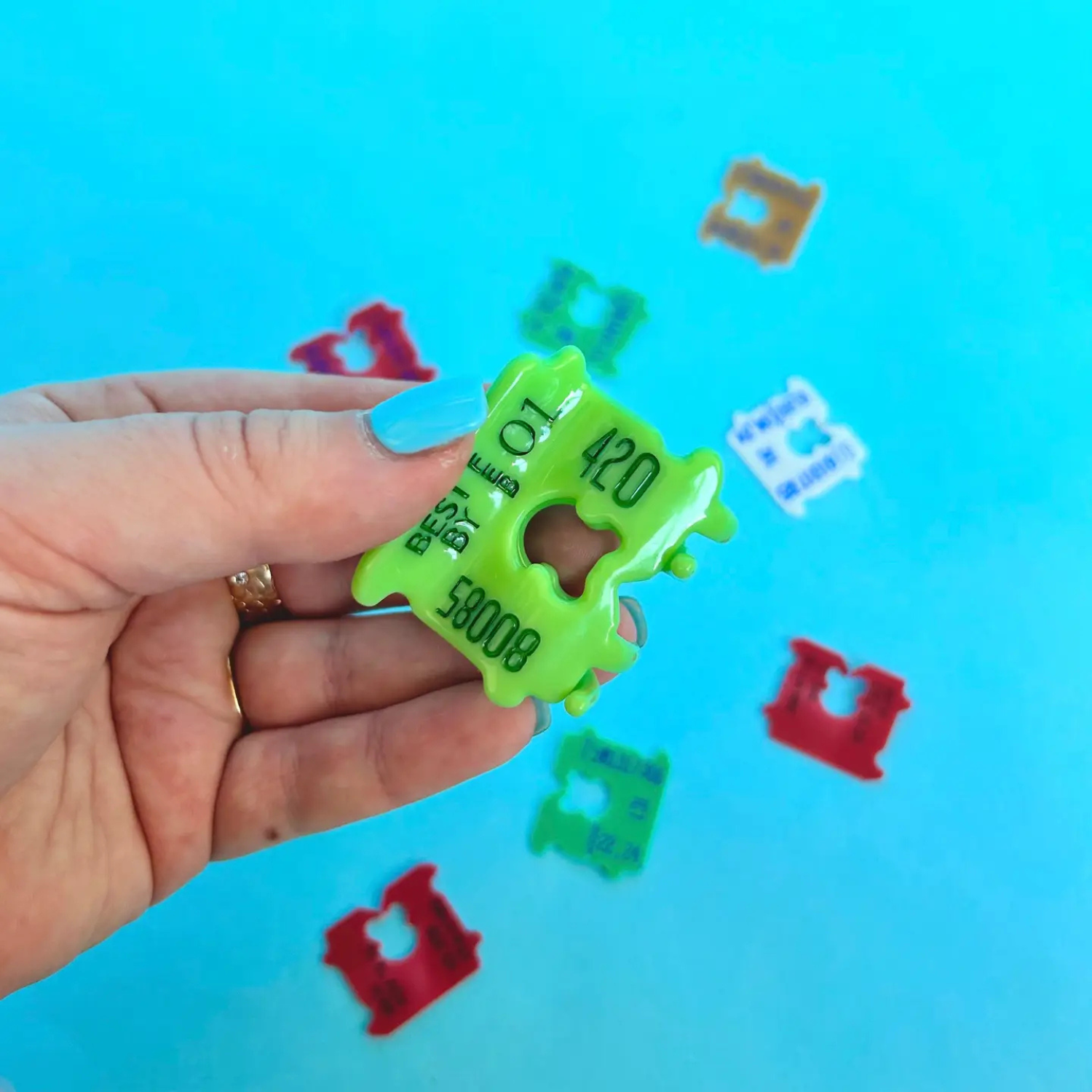 Hand holding a Green plastic hair claw clip that looks like a bread clip against a blue background