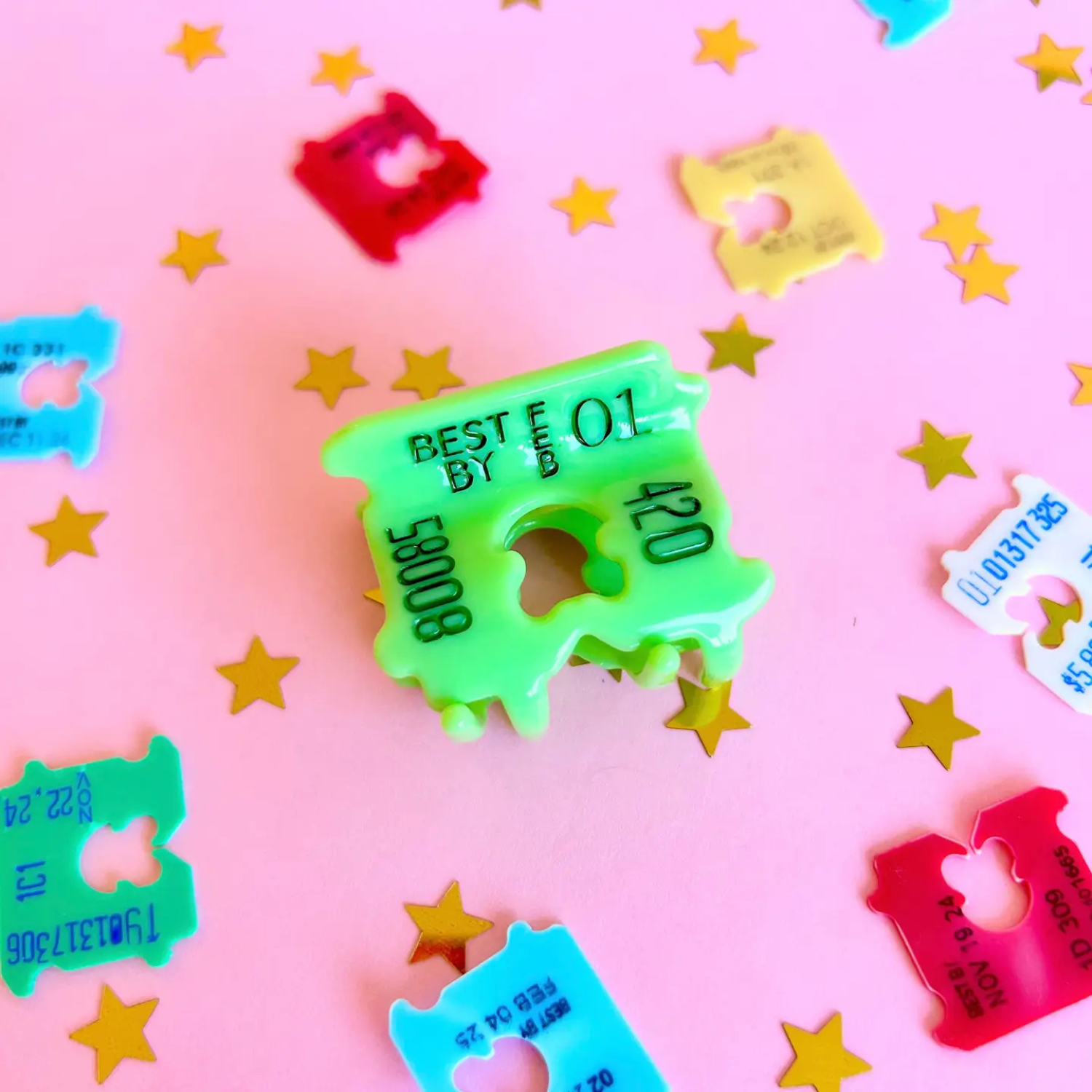 Green plastic hair claw clip that looks like a bread clip surrounded by other bread clips on a pink background with yellow stars