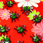 Green and black house fly-shaped pins on a red floral background