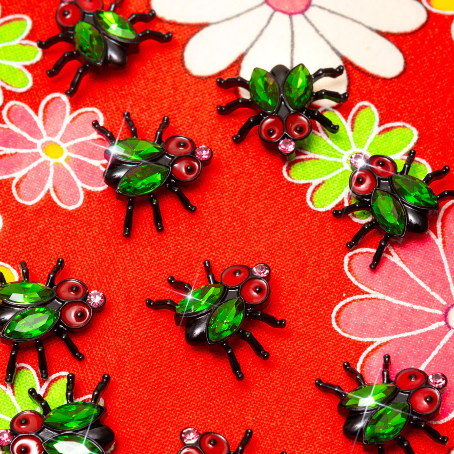 Green and black house fly-shaped pins on a red floral background