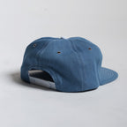 back of blue chambray cap showing adjustable closure on a light gray background