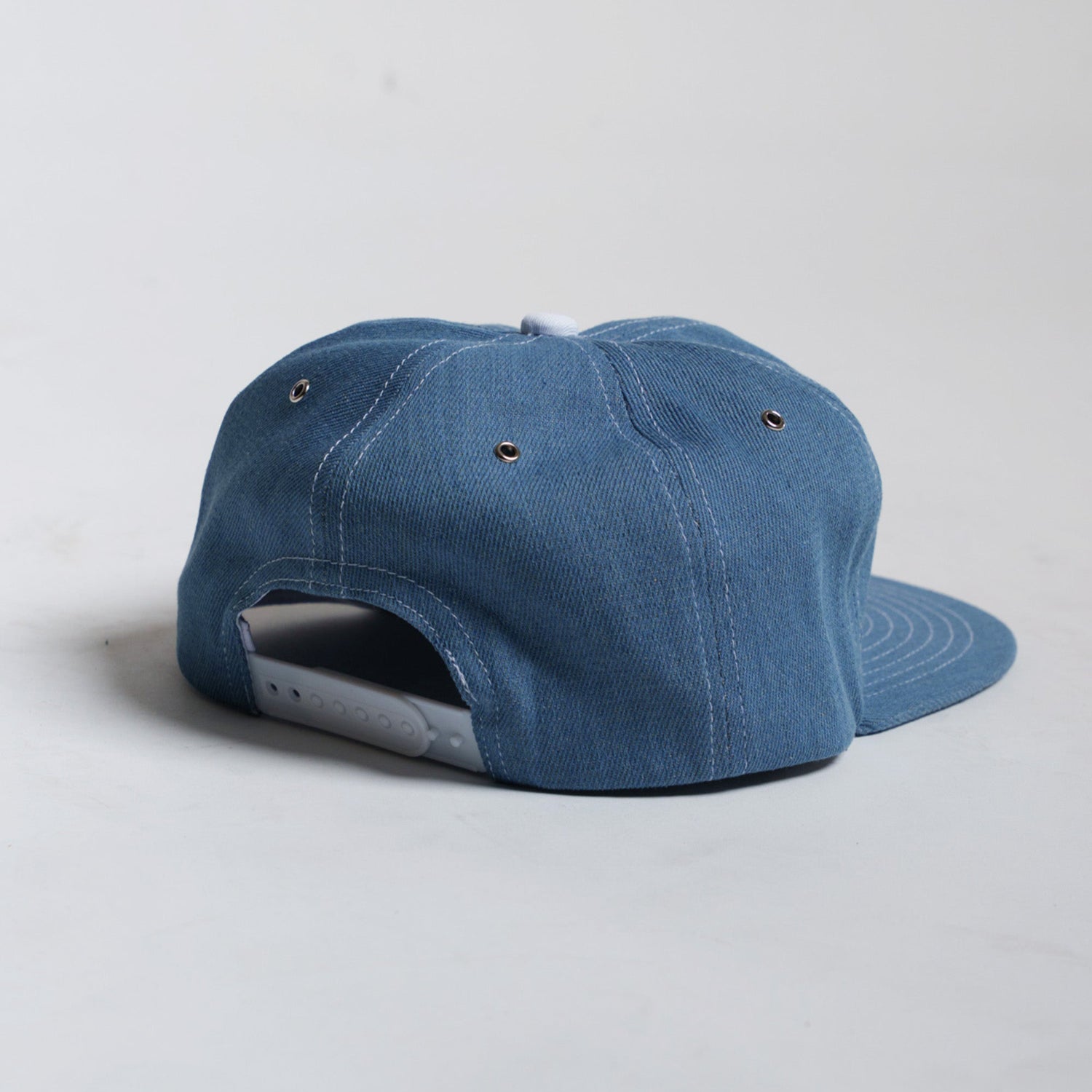 back of blue chambray cap showing adjustable closure on a light gray background