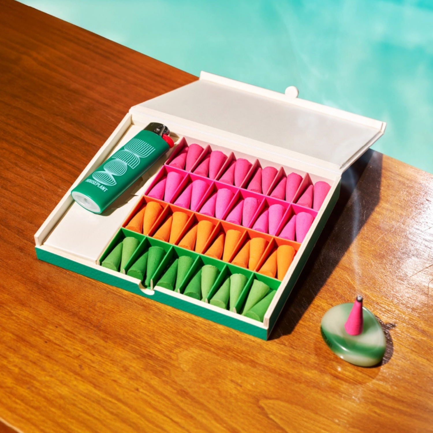 Colorful incense cones in a box with a lighter on a wooden surface by a pool.