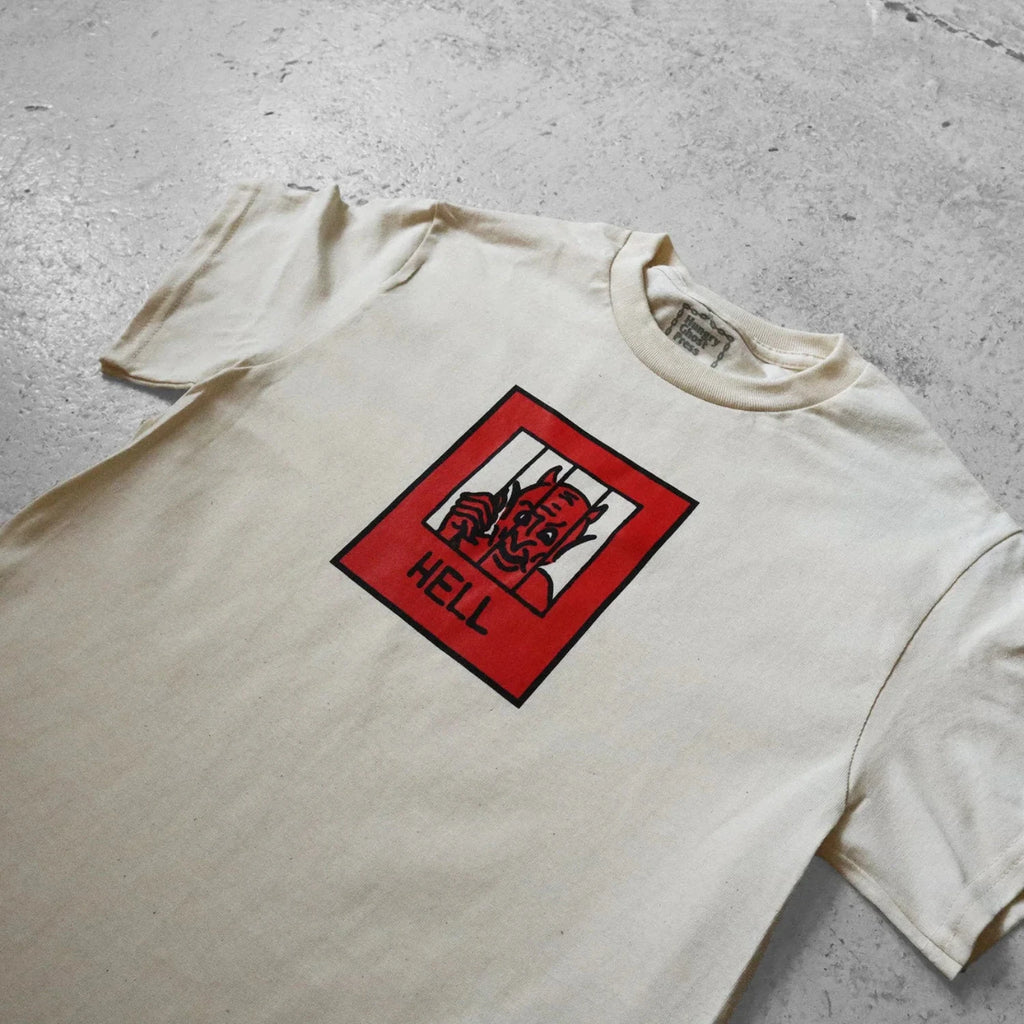 White t-shirt with a graphic design featuring a devil face and 'HELL' text on a red background, laid flat on a concrete surface.