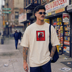 Man wearing a beige t-shirt with a graphic design on a city street.