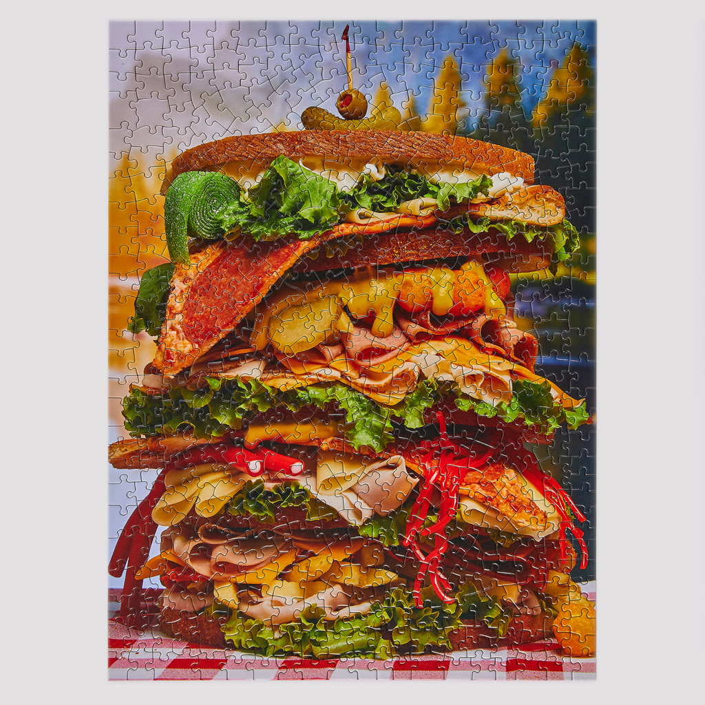 Jigsaw puzzle with a large, detailed illustration of a layered sandwich on a scenic background.