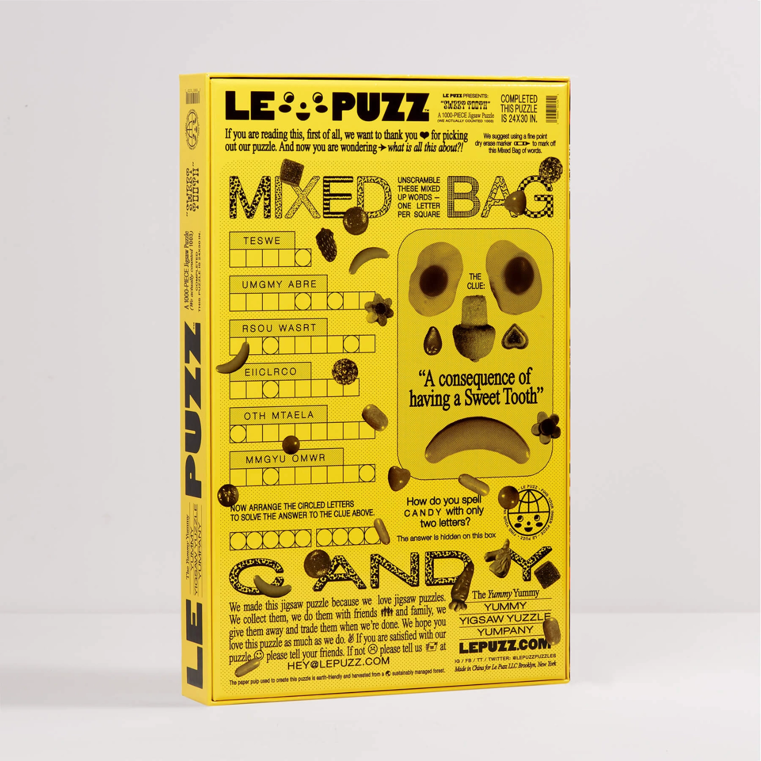 A yellow puzzle book titled 'LE PUZZ' standing upright against a light gray background. The cover features black text, crossword clues, and illustrations of candy and sweets.