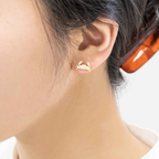 A close-up of a person's ear wearing a small gold crab stud earring, with dark hair and a translucent orange hair tie visible.