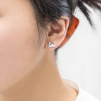 A close-up of a person's ear wearing a small silver stud earring shaped like a crab, with dark hair pulled back and a white top visible.