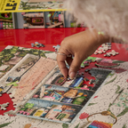 Person assembling a puzzle on a red surface with a magazine in the background