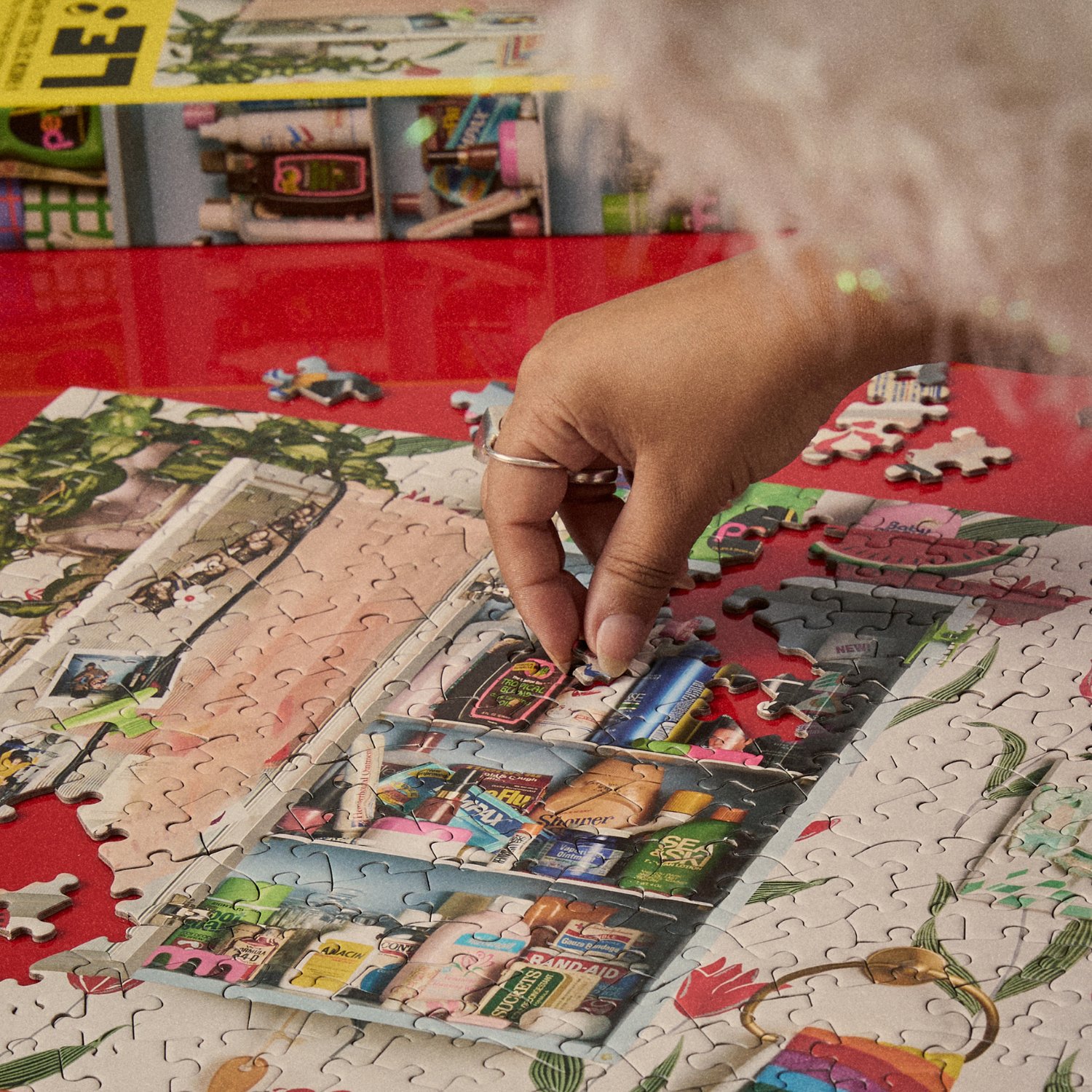 Person assembling a puzzle on a red surface with a magazine in the background