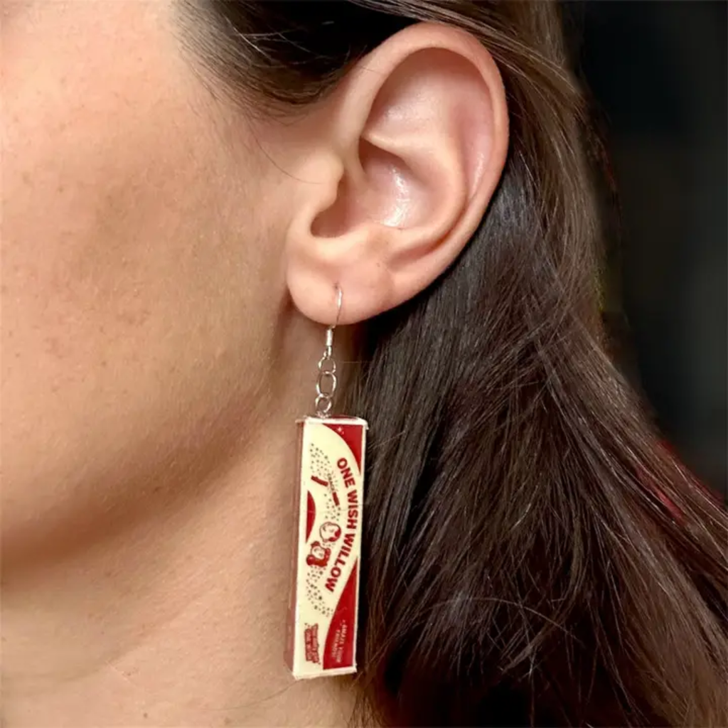 A close-up of a person's ear wearing a dangling earring shaped like a One Wish Willow box from the movie Obsessed.