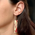 A close-up of a person's ear wearing a dangling earring shaped like a One Wish Willow box from the movie Obsessed.
