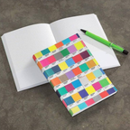 Pantone Color swatch notebook with colorful squares on a gray surface with an open notebook and green pen.