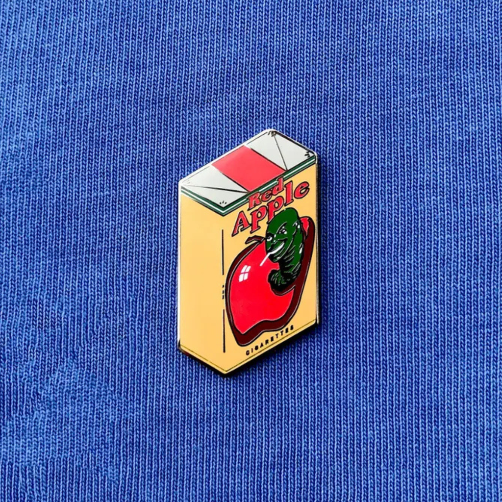 Enamel pin of a Quentin Tarantino Red Apple cigarette pack on a blue fabric background