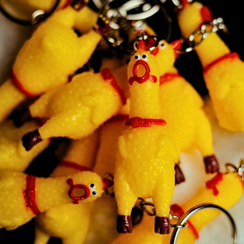 Pile of Yellow chicken keychains with red chokers on a blurred background