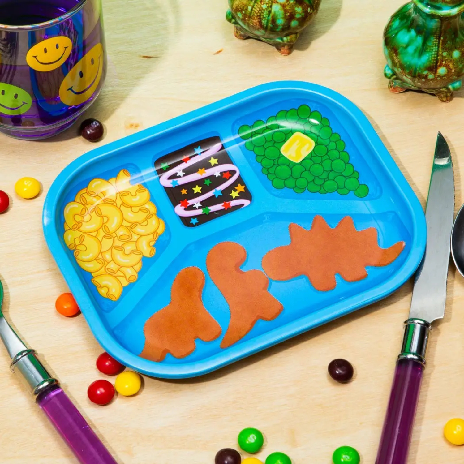 Blue tray designed as a microwave meal with dino nuggets, Mac and cheese, peas, and a brownie on a wooden table with utensils.