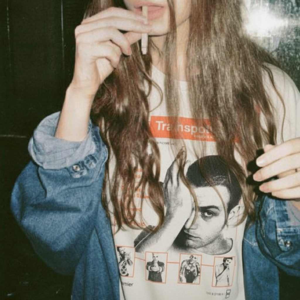 Person wearing a graphic t-shirt with a stylized Trainspotting portrait design, holding a cigarette.