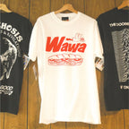 Three t-shirts hanging on a wooden wall with 'Wawa' logo on a white shirt