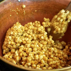 Caramel popcorn in a brown bowl being stirred with a wooden spoon
