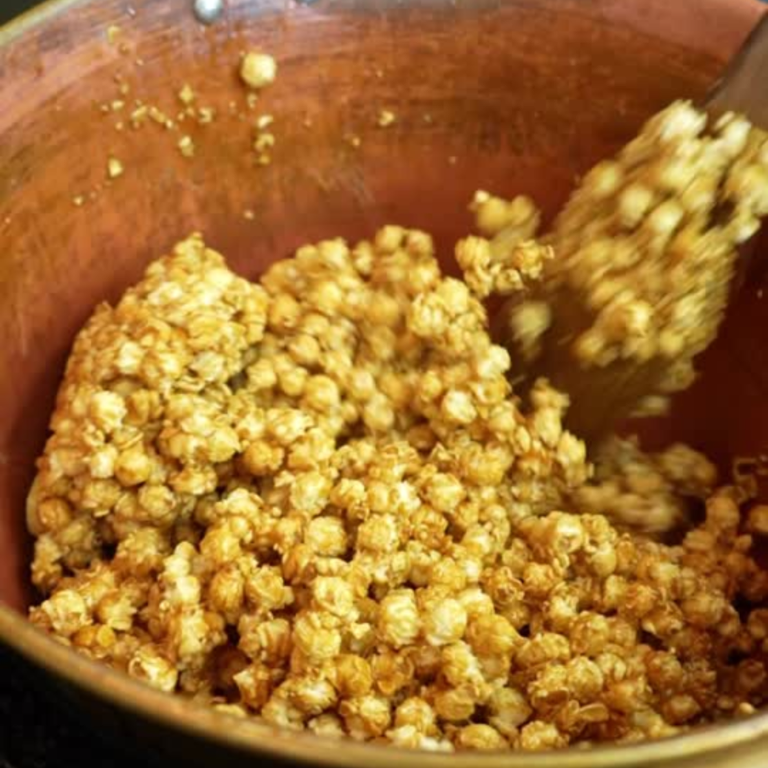 Caramel popcorn in a brown bowl being stirred with a wooden spoon