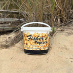 Fisher's Popcorn bucket on a sandy beach with grass and driftwood in the background