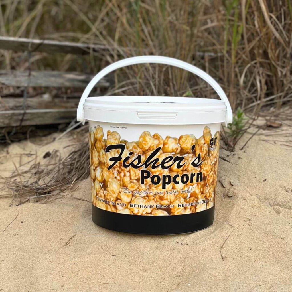 Fisher's Popcorn container on a sandy beach with driftwood in the background