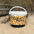 Fisher's Popcorn container on a sandy beach with driftwood in the background