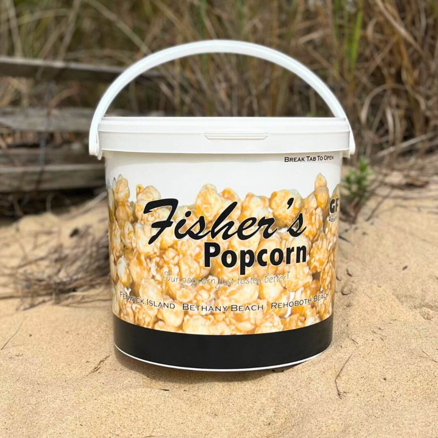 Bucket of Fisher's Popcorn on a sandy surface with grass in the background